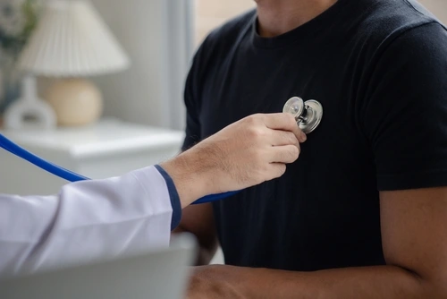 A doctor listens to a man’s heart during an annual physical wellness exam.
