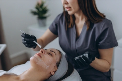 An aesthetician performs a chemical peel treatment on a woman during a facial.