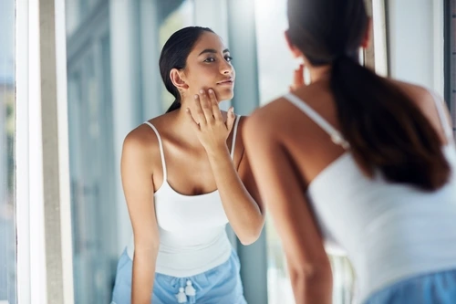A young woman sees clear skin in the mirror after a DiamondGlow dermalinfusion facial.